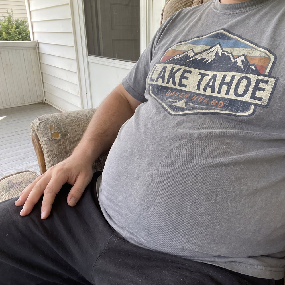 Man sitting on a porch chair with a swollen, firm belly pushing out his t-shirt